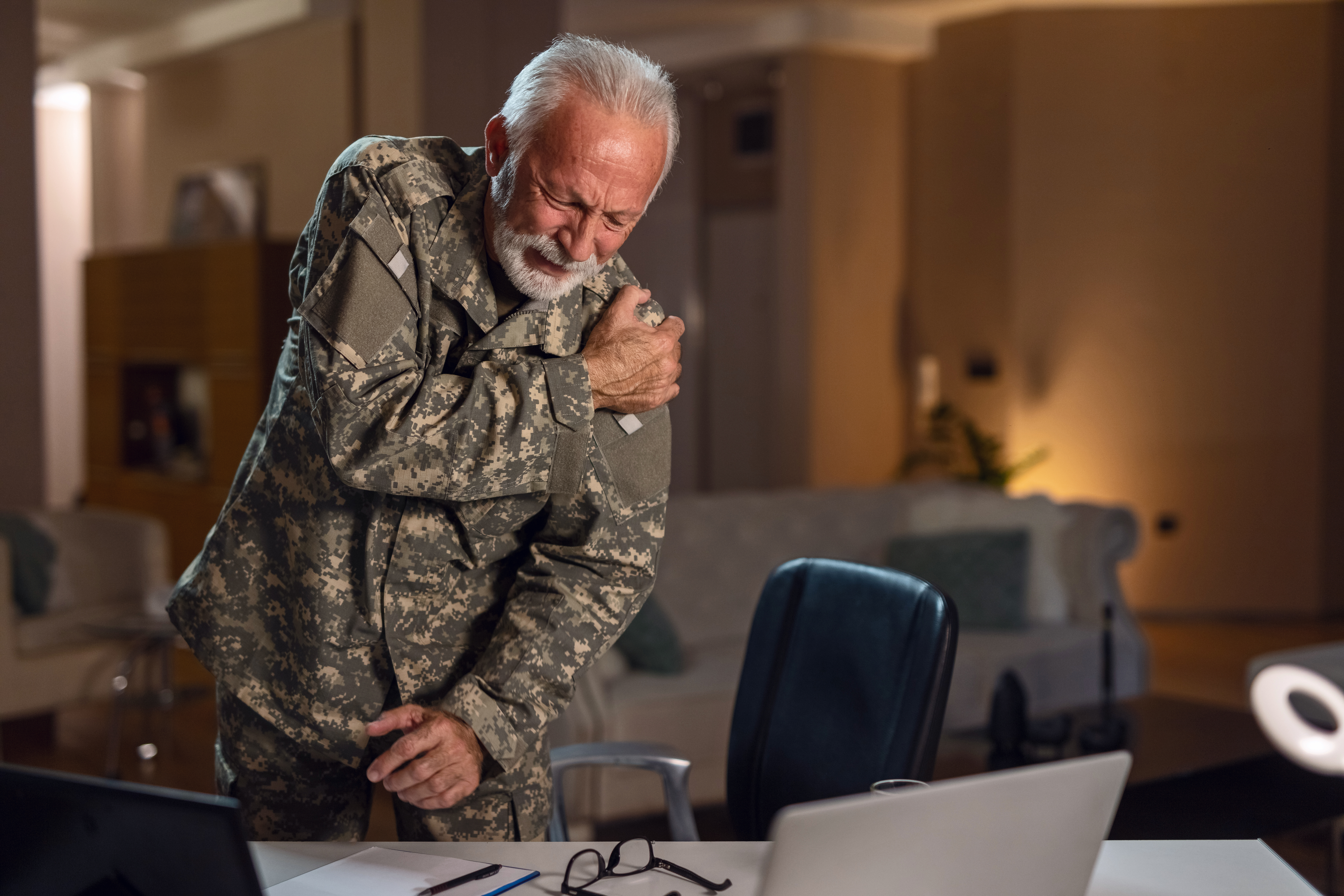 Mature military soldier suffering with fibromyalgia shoulder pain while being in the office.